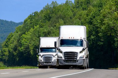 Eyaletler arası yolda fotokopi uzayı olan iki beyaz 18 tekerlekli aracın yatay görüntüsü.