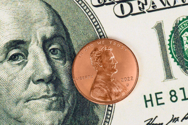 Horizontal shot of an endangered penny on top of a Benjamin Franklin one hundred dollar bill.