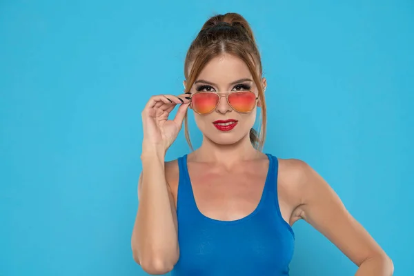 Elegancka Młoda Kobieta Pozująca Okularach Przeciwsłonecznych Niebieskim Tle Studia — Zdjęcie stockowe