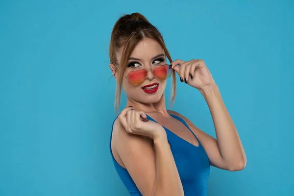 Elegancka Młoda Kobieta Pozująca Okularach Przeciwsłonecznych Niebieskim Tle Studia — Zdjęcie stockowe