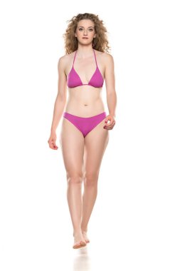 Bikini mayo giymiş genç sarışın kadın beyaz arka planda yürüyor..