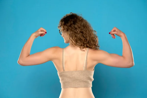 Atraktivní Blondýny Žena Kudrnatými Vlasy Ukazuje Biceps Zpět Modrém Pozadí — Stock fotografie