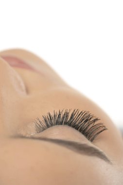 Beyaz stüdyo arka planında kıvrımlı, uzun takma kirpikleri olan kapalı bir kadın gözü.