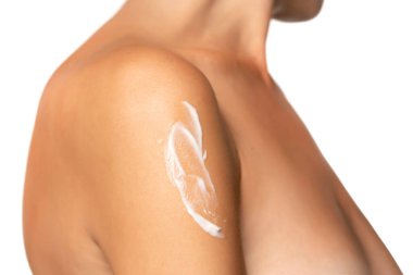 Beyaz stüdyo arka planında krem ile poz veren genç bir kadın.