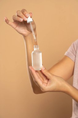 female hands holding bottle and pipette on beige studio background
