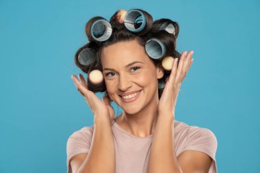 Beautiful smiling woman with hair curlers posing on a blue studio  background