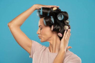 Beautiful smiling woman with hair curlers posing on a blue studio  background. Profile view.