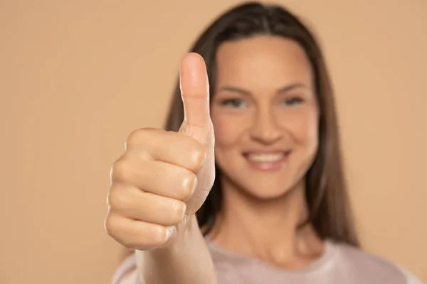 照片上的年轻快乐女人在米色工作室的背景下竖起大拇指 — 图库照片