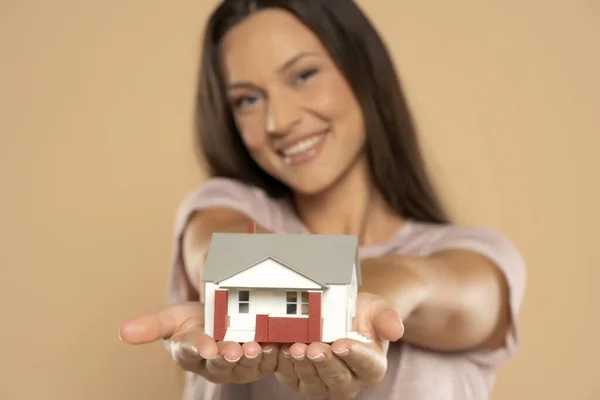 Young woman smiling and holding house sample model isolated over beige studio background, Real estate and home insurance concept