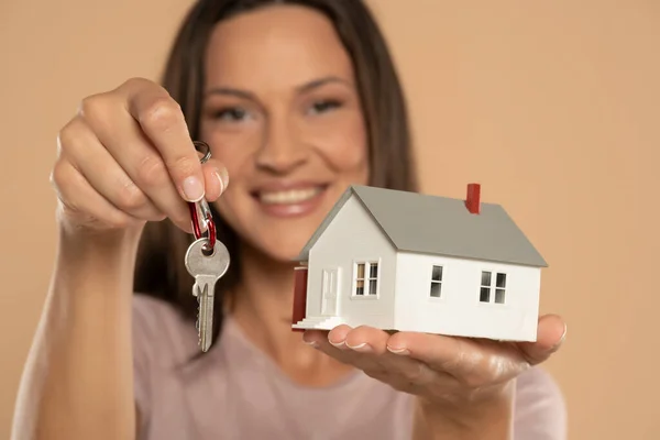 Young Woman Smiling Holding House Sample Model Keys Isolated Beige — Stockfoto