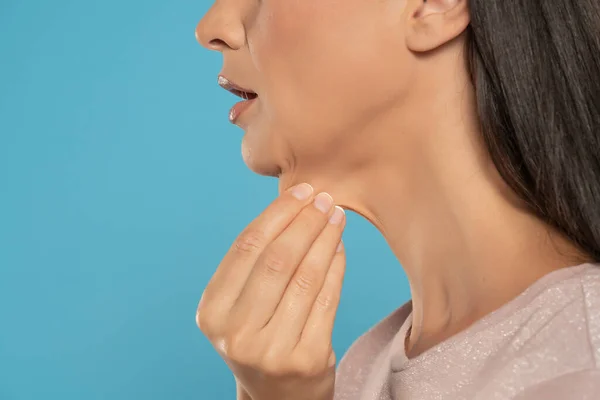 A close-up and side profile view of a caucasian lady pinching the loose skin at the front of her throat. Commonly called a turkey neck and corrected with a platysmaplasty