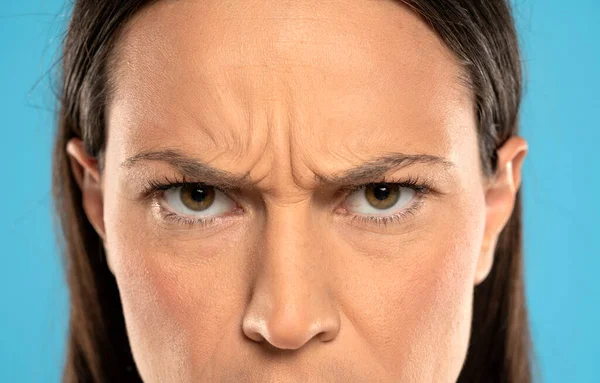 Angry face of a young woman with facial wrinkles closeup on a blue background