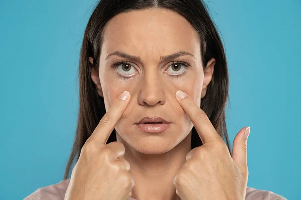 Young Woman Pulling Her Lower Eyelids Her Fingers Blue Studio — Stock Photo, Image