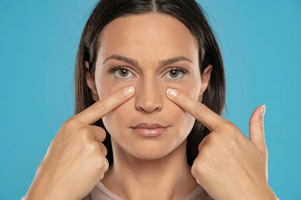Mujer Toca Cara Bajo Sus Ojos Fondo Azul Estudio —  Fotos de Stock