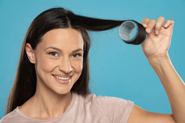 Young Woman Putting Curlers Her Hair Blue Studio Background — Fotografie, imagine de stoc