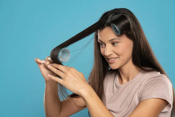 Young Woman Putting Curlers Her Hair Blue Studio Background — Foto Stock
