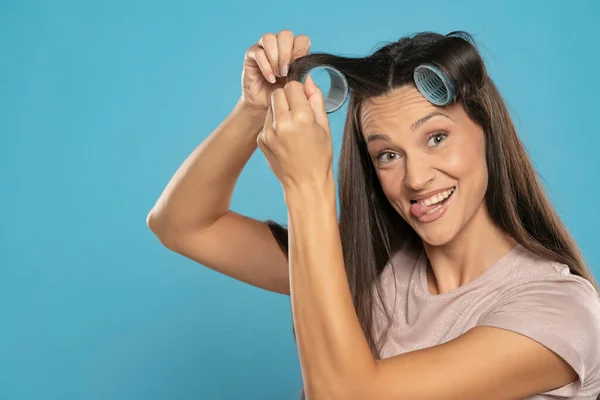 Young Woman Putting Curlers Her Hair Blue Studio Background — Stockfoto