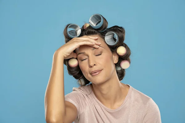 Beautiful bored woman with hair curlers on a blue studio  background