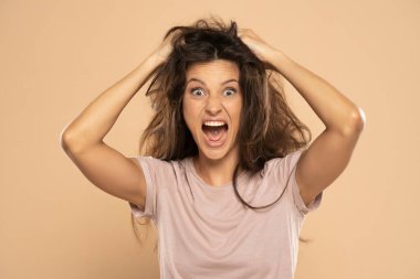 Angry nervous woman pulling her messy long hair on a beige studio background