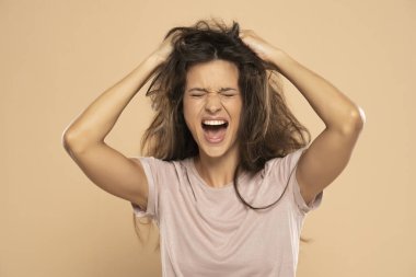 Angry nervous woman pulling her messy long hair on a beige studio background