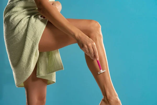 Woman shaves her legs on blue studio background