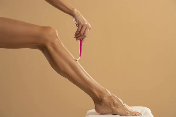Woman Shaves Her Legs Beige Studio Background —  Fotos de Stock