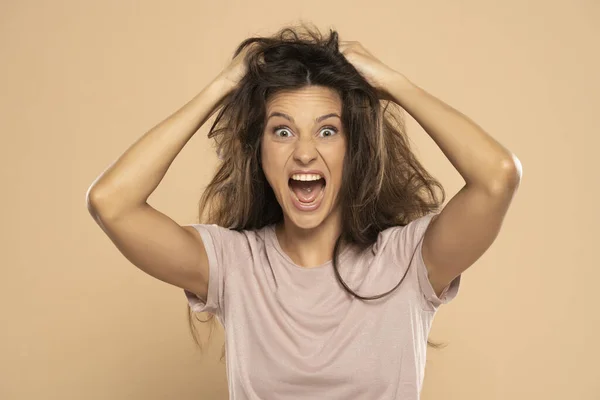 愤怒而紧张的女人在米色的工作室背景下拉着乱蓬蓬的长发 — 图库照片