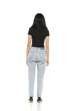 Back view of a young woman in loose jeans posing on white studio background