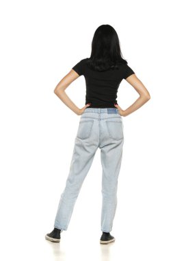 Back view of a young woman in loose jeans posing on white studio background