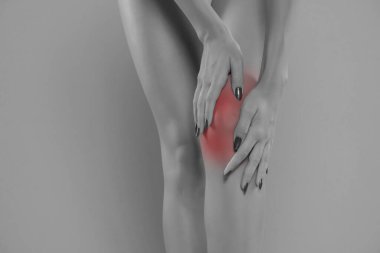 woman holding her painful knee on blue studio background.
