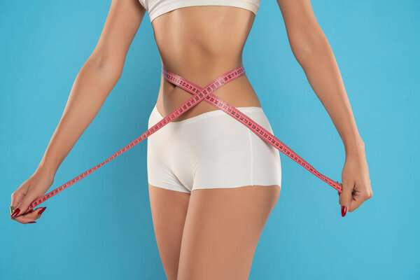 Женщина измеряет свою талию на синем фоне студии. Поражение стройного тела