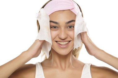 Çekici, gülümseyen genç bir kadın beyaz stüdyo arka planında ıslak bir mendille yüzünü temizliyor.