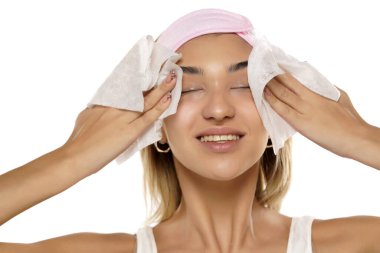 Çekici, gülümseyen genç bir kadın beyaz stüdyo arka planında ıslak bir mendille yüzünü temizliyor.