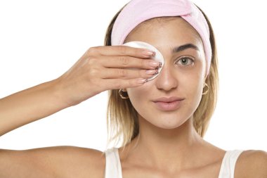 Çekici, gülümseyen genç bir kadın beyaz stüdyo arka planında ıslak bir mendille yüzünü temizliyor.