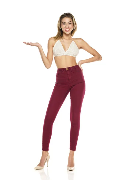 Smiling Woman Burgundy Jeans Top Presenting Something Her Empty Palm — Stok Foto