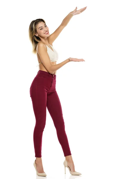 Smiling Woman Burgundy Jeans Top Presenting Something Her Empty Palm — Stok Foto