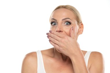 Orta yaşlı, utangaç, makyajlı, elini beyaz stüdyo arka planına sürmüş bir kadının portresi.