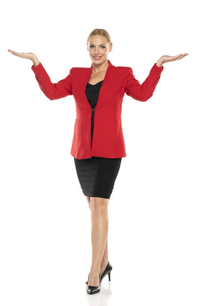 Middle aged advertising senior business woman in red jacket and black skirt posing on white studio background. Front view.