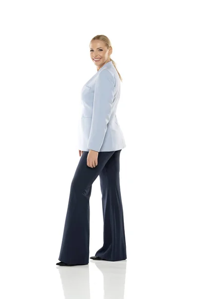 白いスタジオの背景に青いジャケットと黒いズボンを着た中年の笑顔の女性 サイドビュー — ストック写真