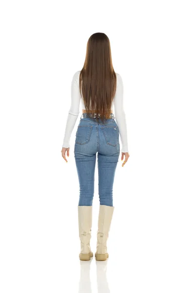 バック 白いシャツの若い女性のリアビュー 白いスタジオの背景に青いジーンズとブーツ — ストック写真