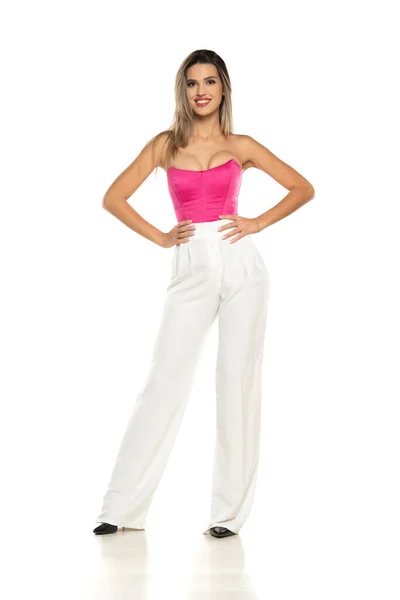 若いです現代的な笑顔女性で白いパンツとピンクのコルセットポージング上の白いスタジオの背景 — ストック写真