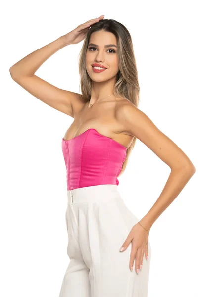 若いです現代的な笑顔女性で白いパンツとピンクのコルセットポージング上の白いスタジオの背景 — ストック写真