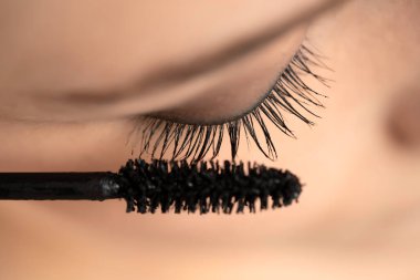 Makro, beyaz bir stüdyo arka planında rimel süren genç bir kadının yakın çekimi.