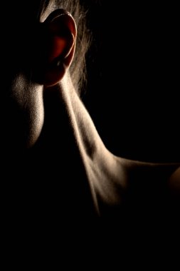 Karanlık stüdyo arka planında gölgede genç bir kadının boynunun yakın çekimi.