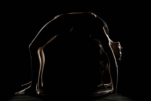 Art silhouette of a young woman doing yoga exercise. Yoga pose on black studio background.