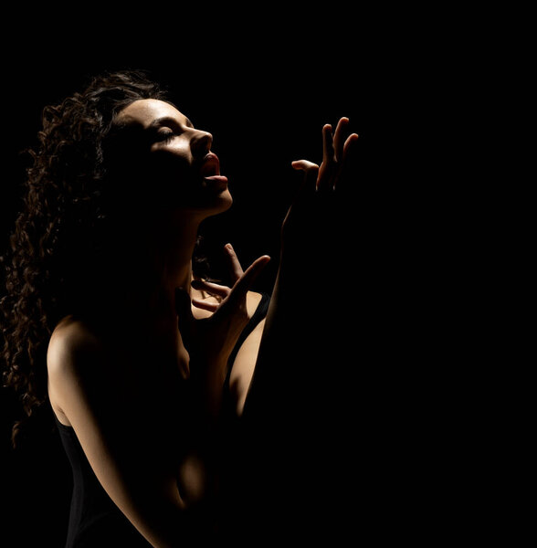 Sensual portrait silhouette of beautiful curly woman with outstretched hand sings in backlight on a black studio background