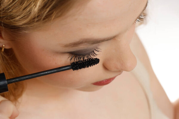 closeup of a young woman applying mascara on a white studio background