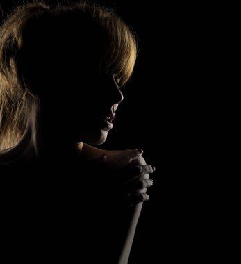 Siyah bir stüdyoda omzuna dokunan genç bir kadının silüeti.