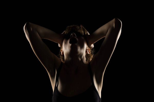 Portrait of a screaming woman in the shadow, hold her head , closed eyes on a black studio background