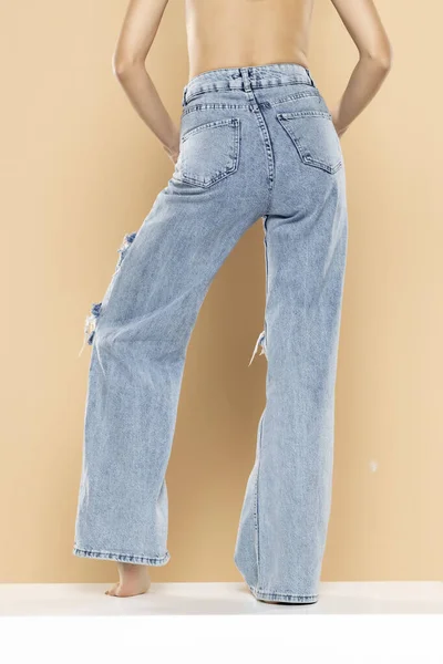 Pernas Uma Mulher Jeans Rasgado Fundo Estúdio Bege Voltar Visão — Fotografia de Stock
